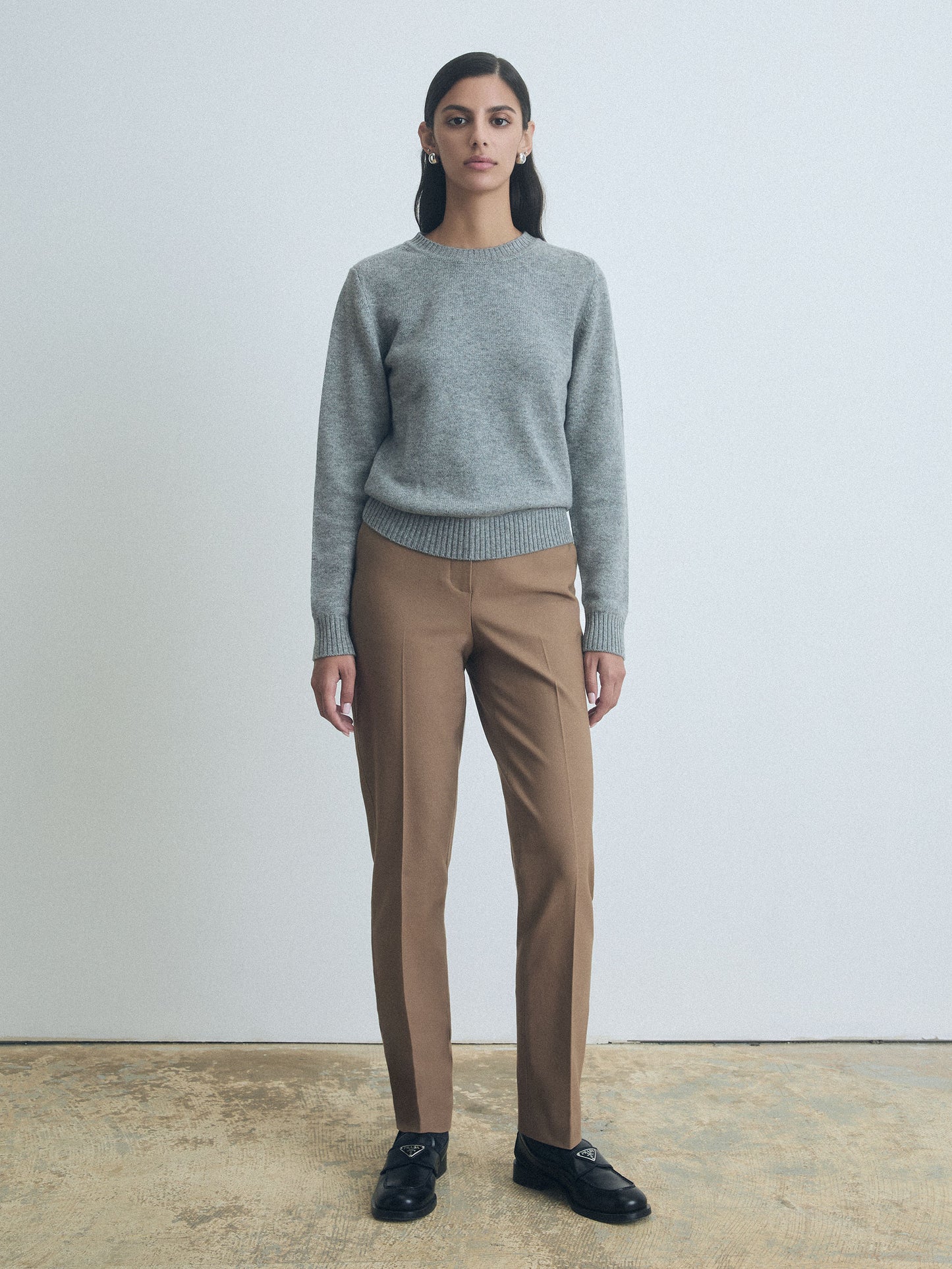 Person wearing a gray sweater and camel judith and charles pants standing against a plain background