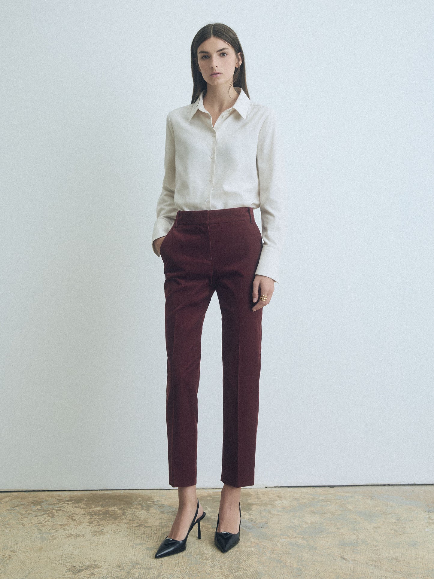 Woman wearing Cream Jennifer blouse by Judith & Charles, long cotton sleeve, classic fit, shirt collar, front button closure, and rust pants against a plain background