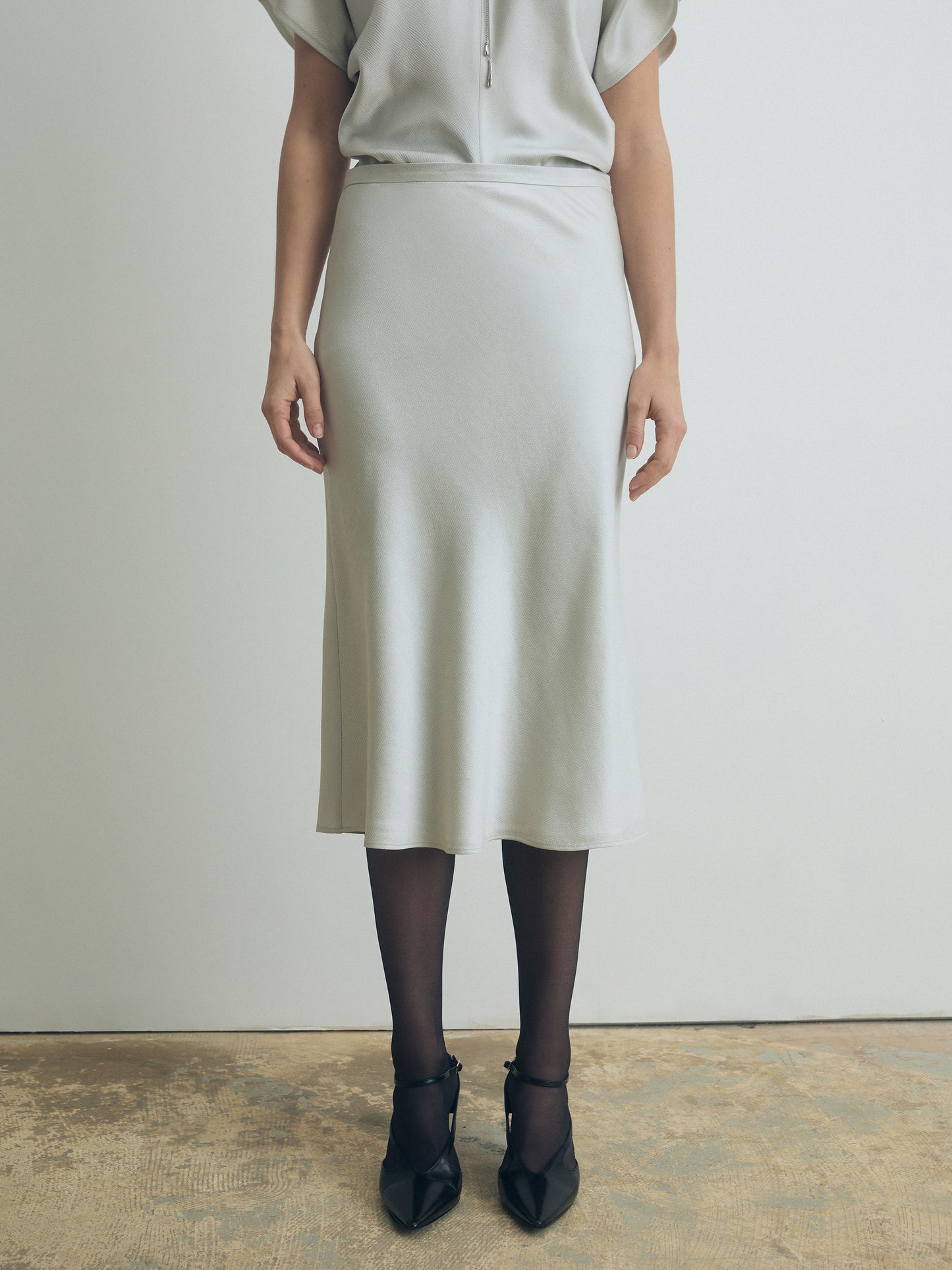 Person wearing a light-colored pearl skirt and top against a plain background