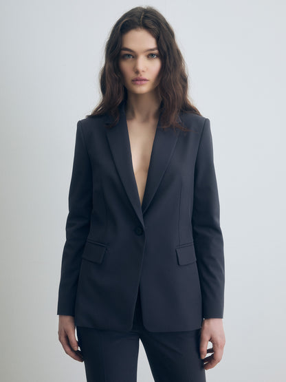 Tailored dark grey jacket with a single-breasted design, sharp peak lapels, and structured shoulders, paired with matching trousers. The jacket features a single button closure and flap pockets, creating a sleek, modern silhouette.