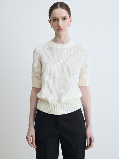 Woman wearing a white textured sweater and black pants on a light gray background