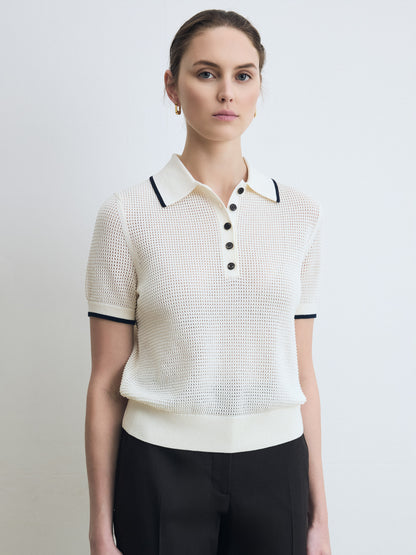 Woman wearing a white textured polo shirt with black trim on a plain background