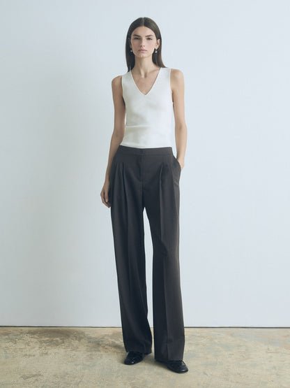 Woman wearing a white sleeveless top and black wide-leg pants against a plain background