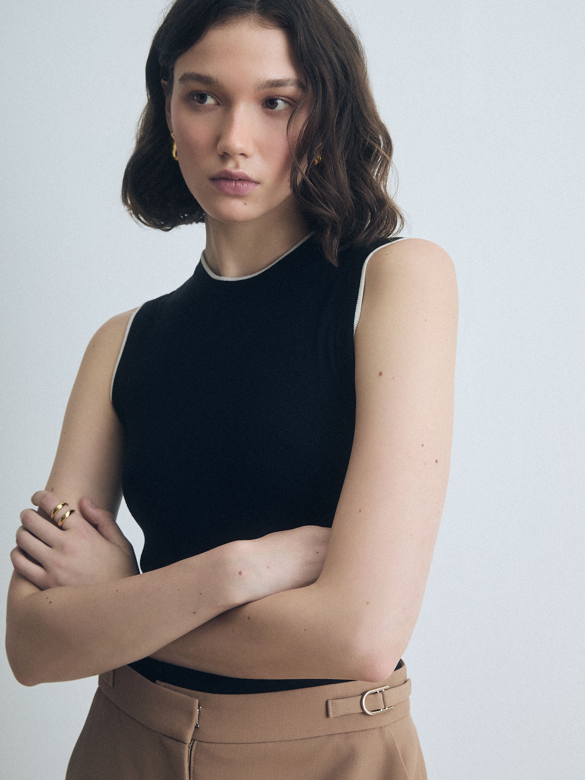 Woman wearing a Black and Off White Crew Neck Shell With White Tipping by Judith & Charles top and camel pants against a plain background