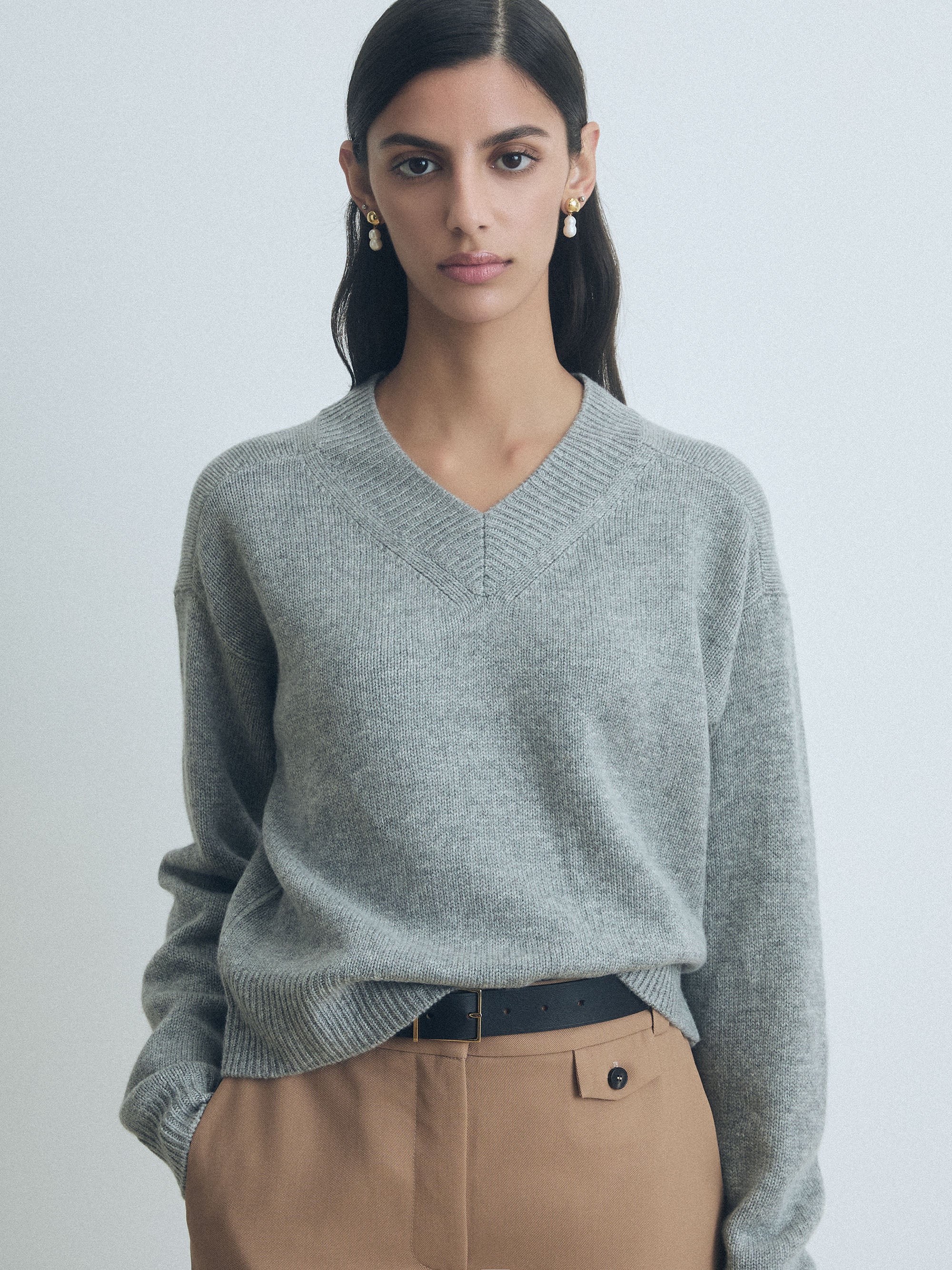 Woman wearing a light grey cashmere high V-neck sweater by Judith & Charles with arms crossed against a light background