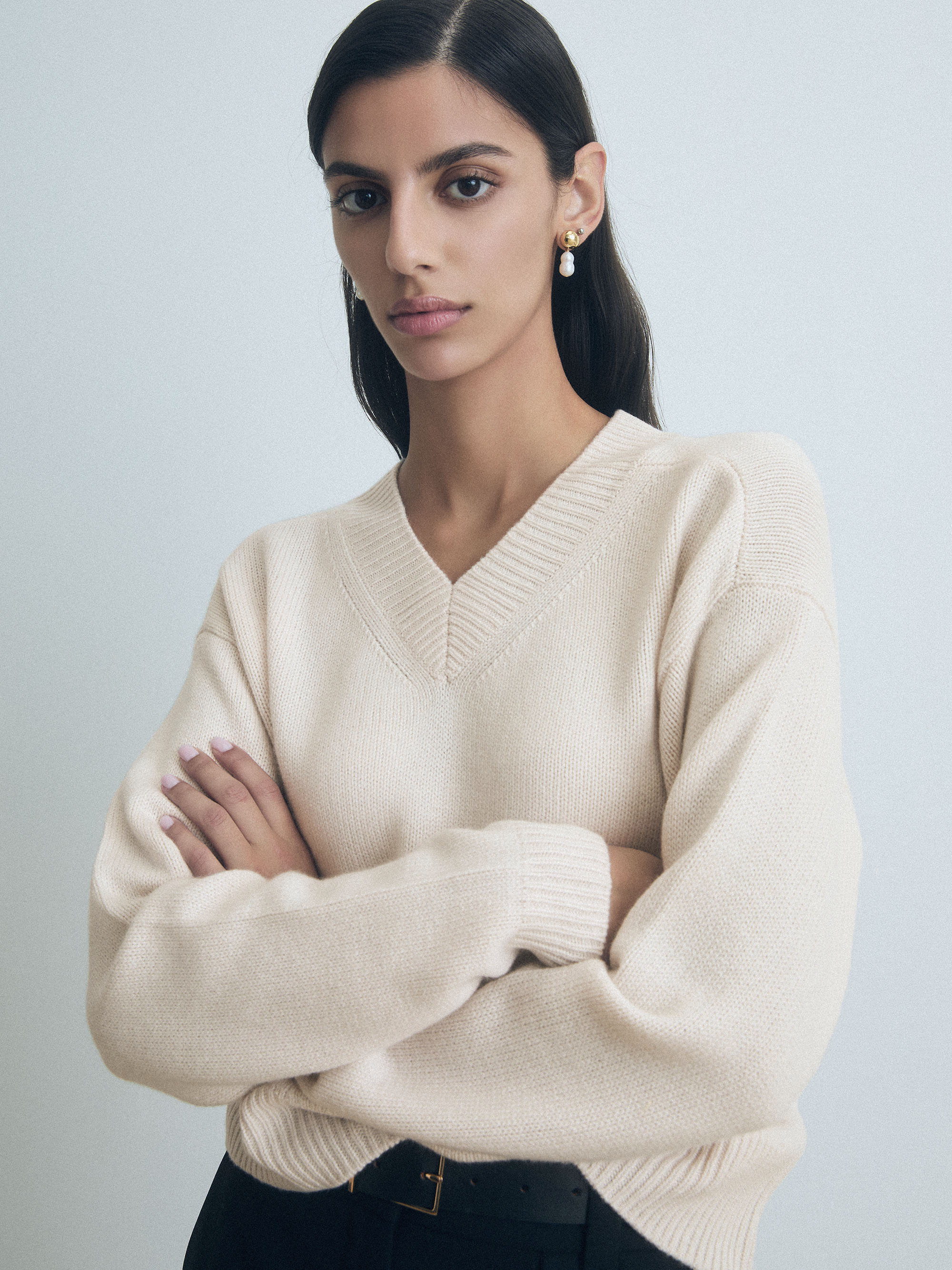 Woman wearing a Sand wool-cashmere high V-neck sweater by Judith & Charles. sweater with arms crossed against a light background