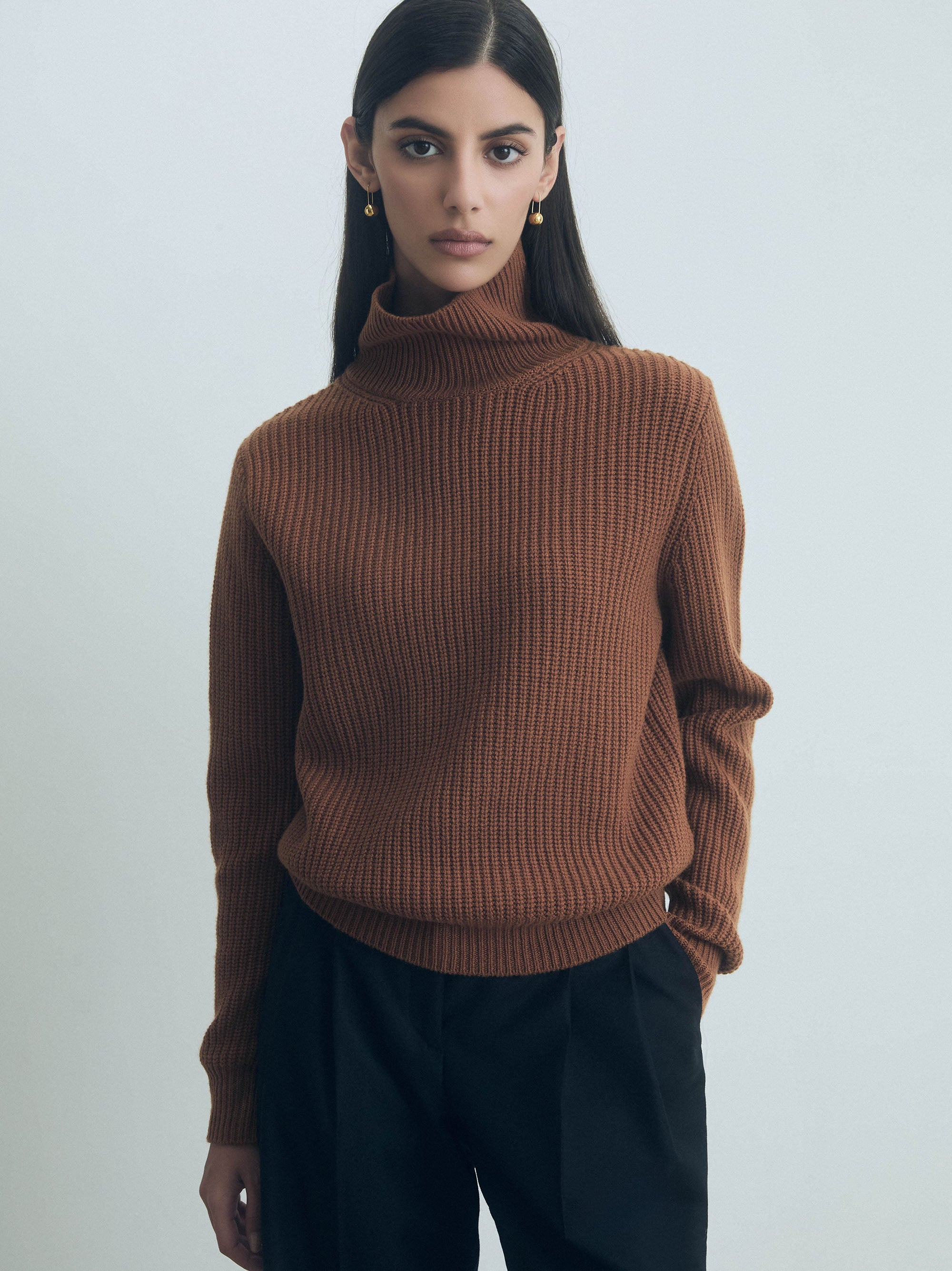 Woman wearing a Vicuna Corey turtleneck sweater by Judith & Charles, made from 70% wool and 30% cashmere, fisherman rib knit turtleneck sweater against a plain background