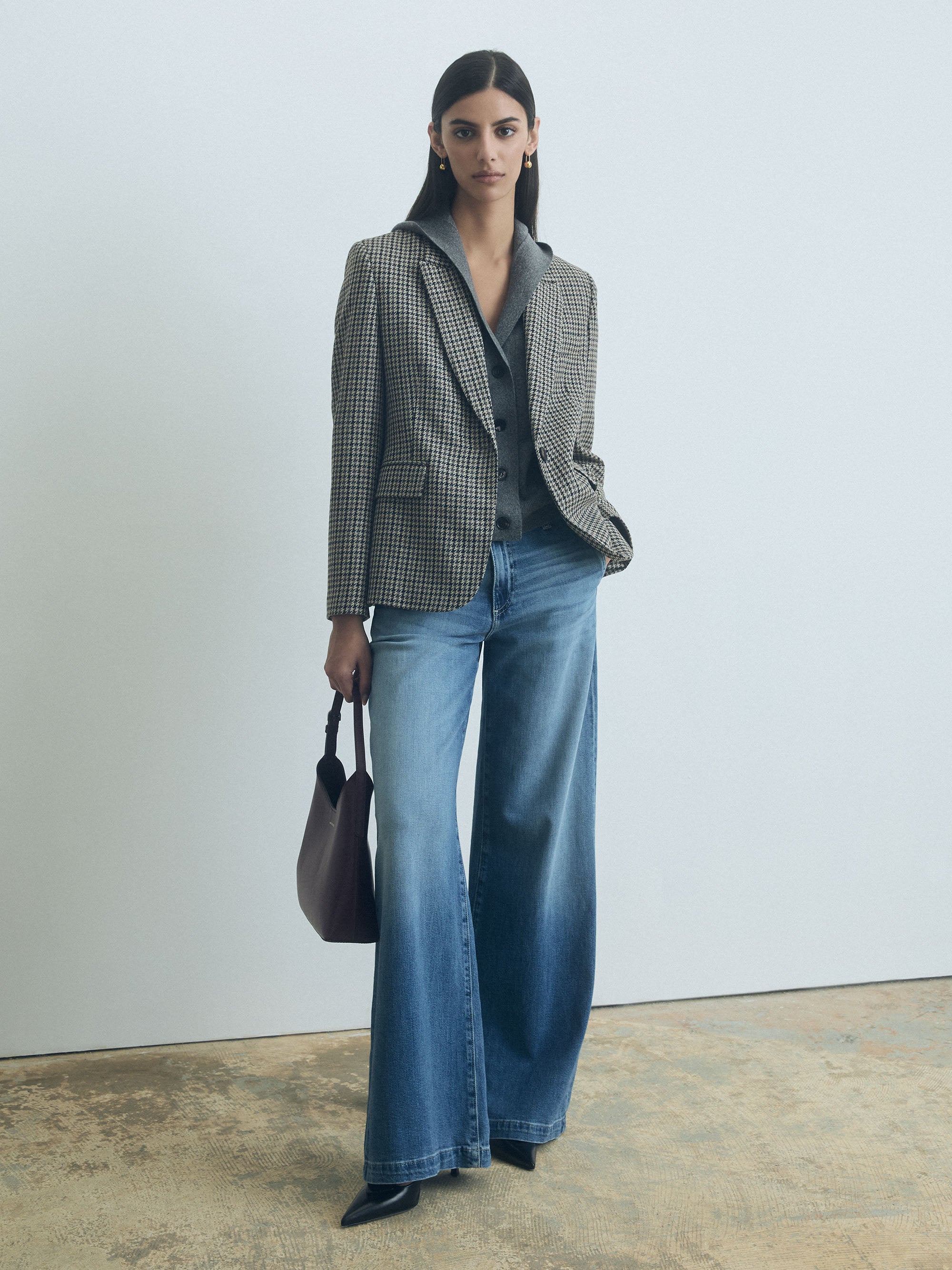 Woman wearing a Grey Melange sleeveless hooded wool-cashmere vest with button front closure by Judith & Charles and blue jeans against a plain background