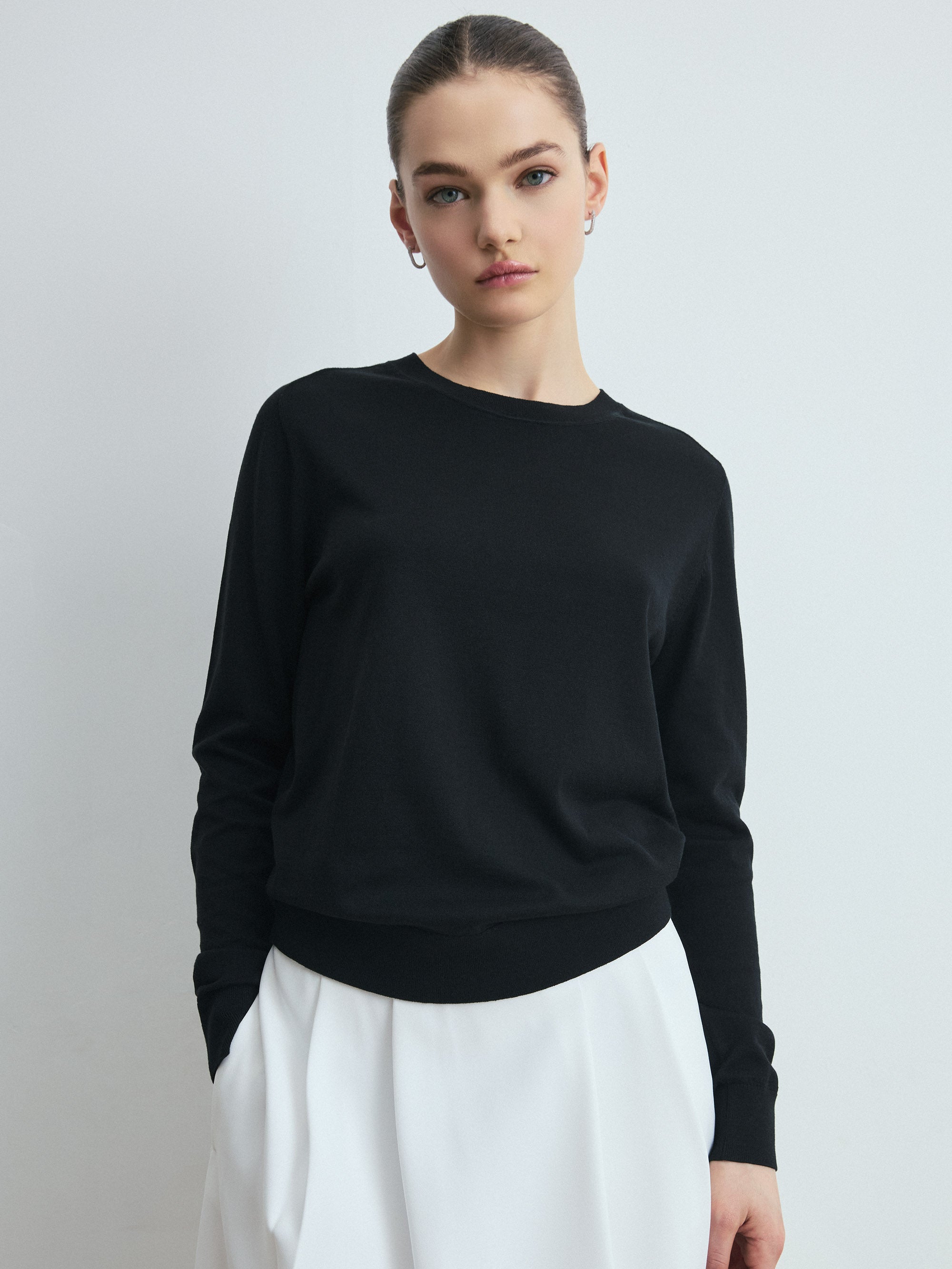 Black silk‑cotton crewneck sweater styled with long sleeves and paired with white wide‑leg trousers.