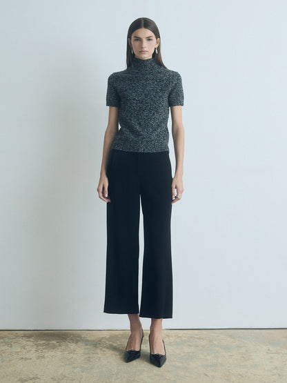 Woman wearing a patterned turtleneck and black wide-leg pants against a plain background