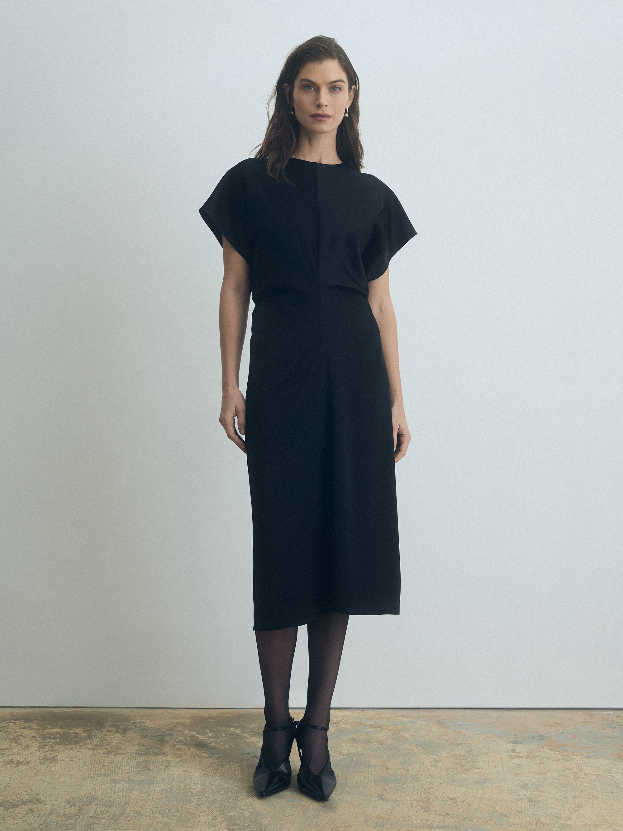Woman wearing a black dress standing against a plain background