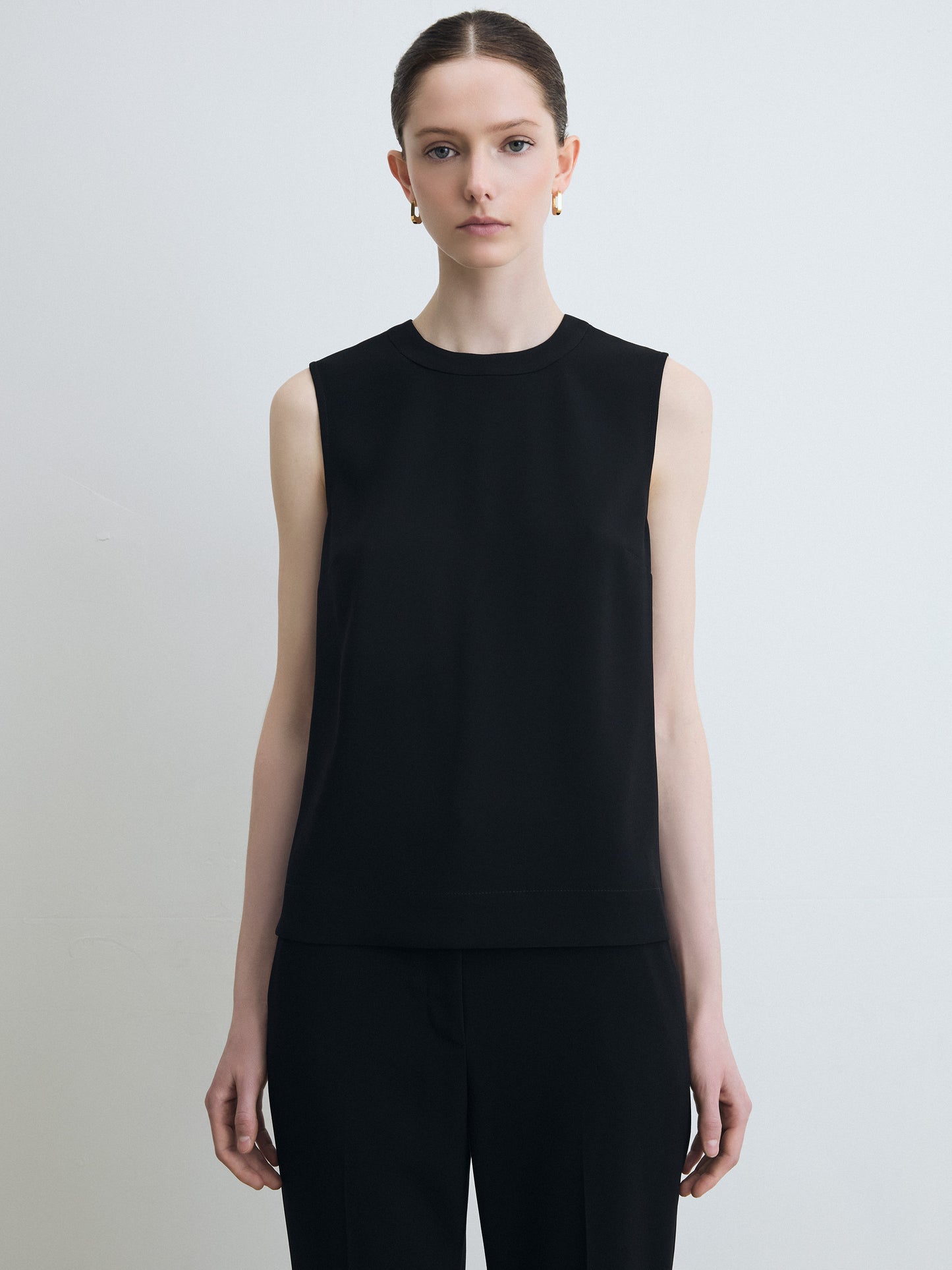 Person wearing a black sleeveless top against a plain background