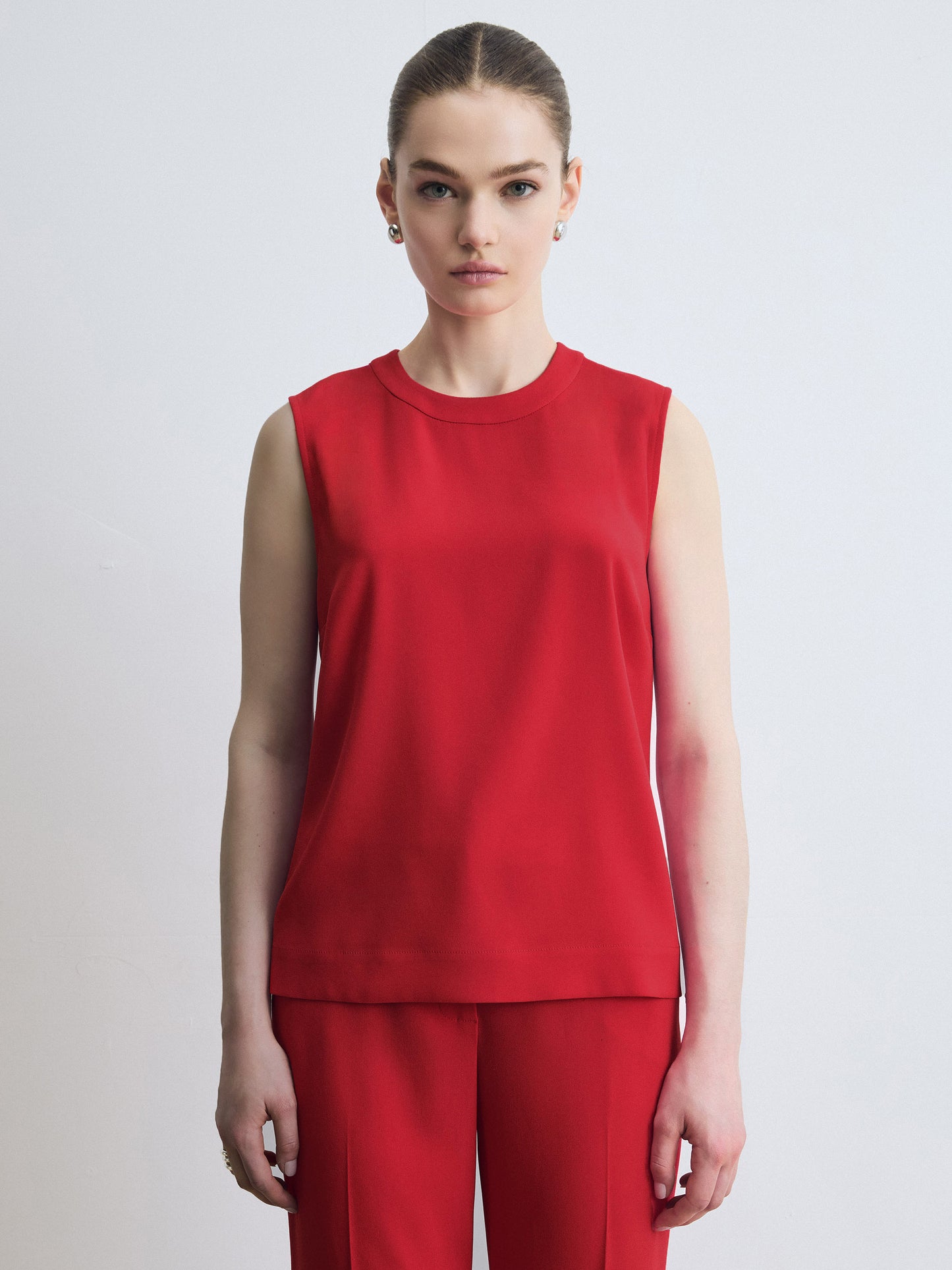 Person wearing a red sleeveless top and pants on a light gray background
