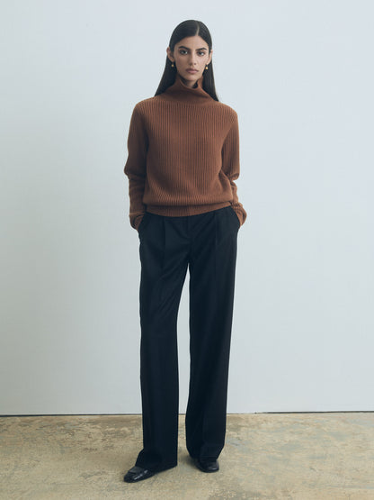 Woman wearing a sweater and judith and charles black pleated pants against a plain background