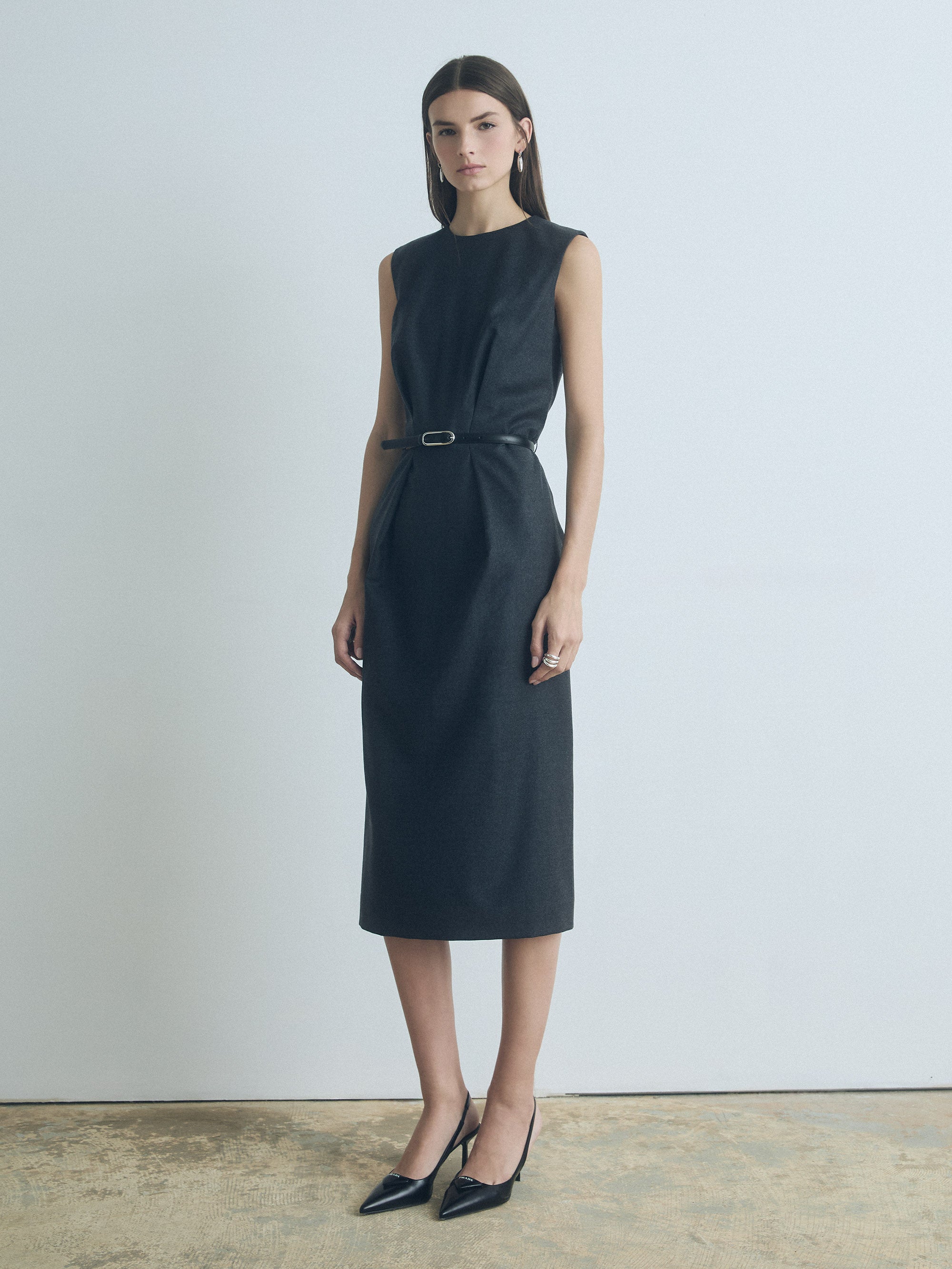 Woman wearing a Dark Grey Melange sleeveless wool dress with crew neck, leather belt, and back slit by Judith & Charles.