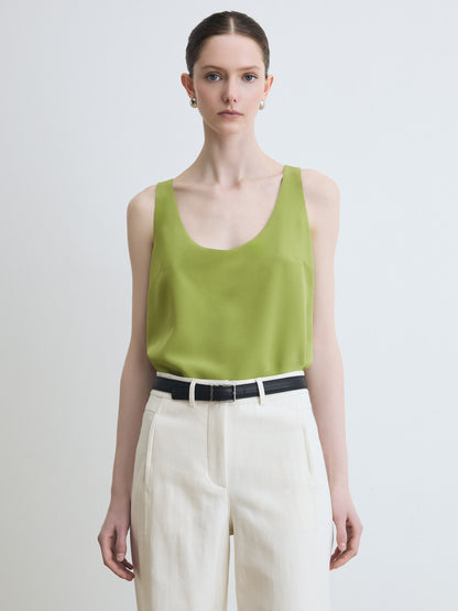 Woman wearing a green sleeveless top and beige pants on a plain background