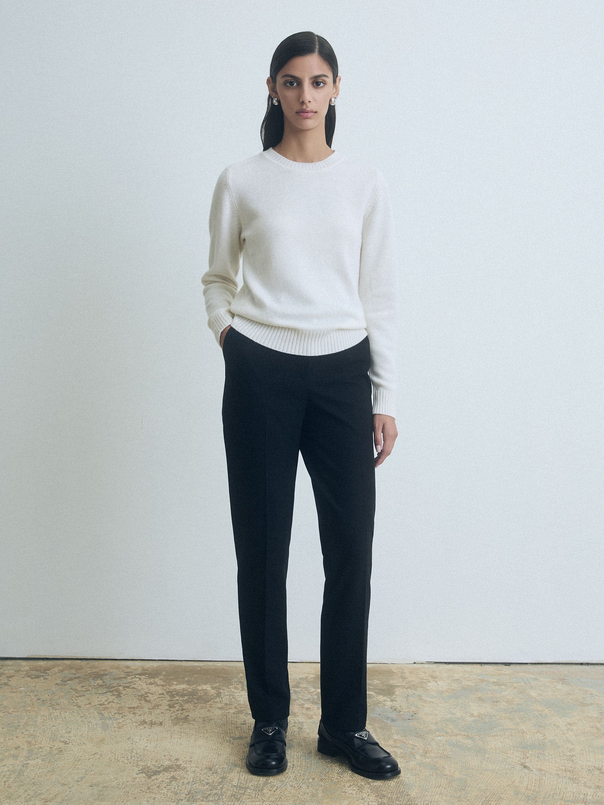 Person wearing a sweater and black judith and charles pants against a plain background