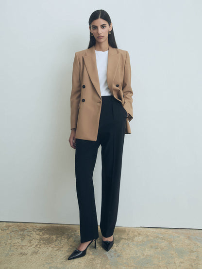 Woman wearing a camel blazer, white shirt, and black judith and charles pants against a plain background