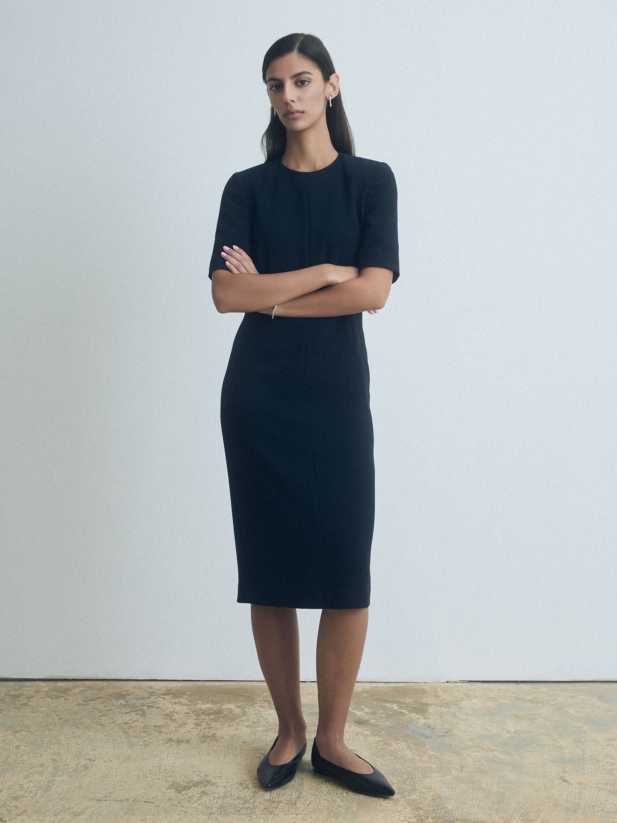 Woman wearing a navy dress standing against a plain background