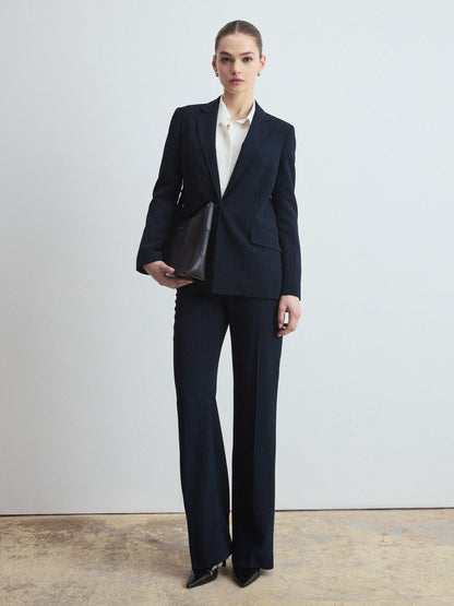 Person wearing a navy stripe suit with a white shirt, holding a black handbag on a plain background