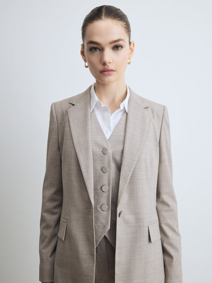 Close-up of a taupe melange tailored jacket worn over a matching buttoned waistcoat and white shirt, showing the notch lapel and flap pockets