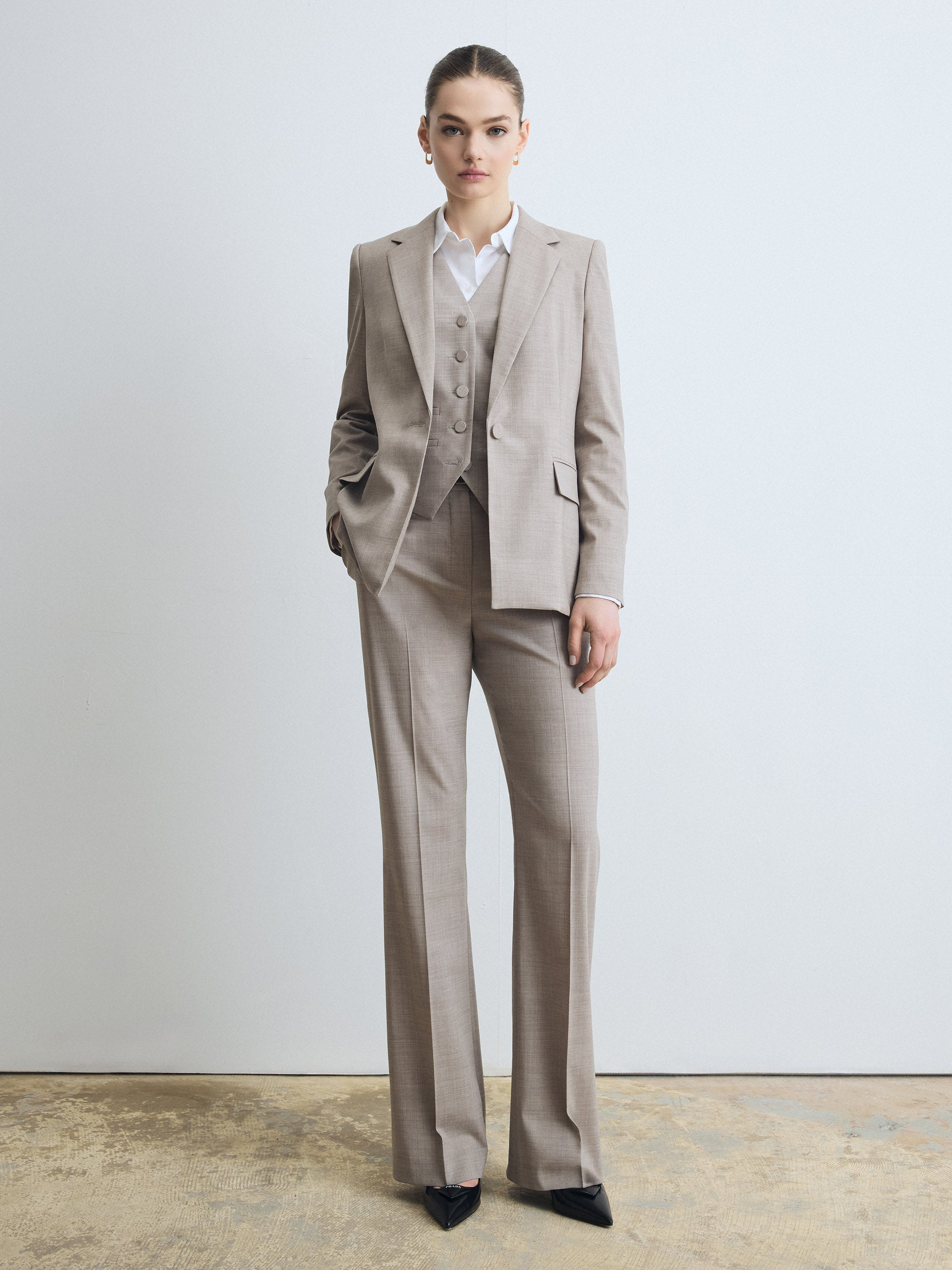 Tailored three‑piece suit in taupe melange wool featuring a single‑button jacket with notch lapel, matching waistcoat, and straight‑leg trousers, styled with a white shirt.