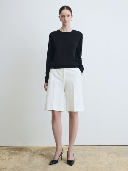 Woman wearing a black sweater and white shorts on a plain background