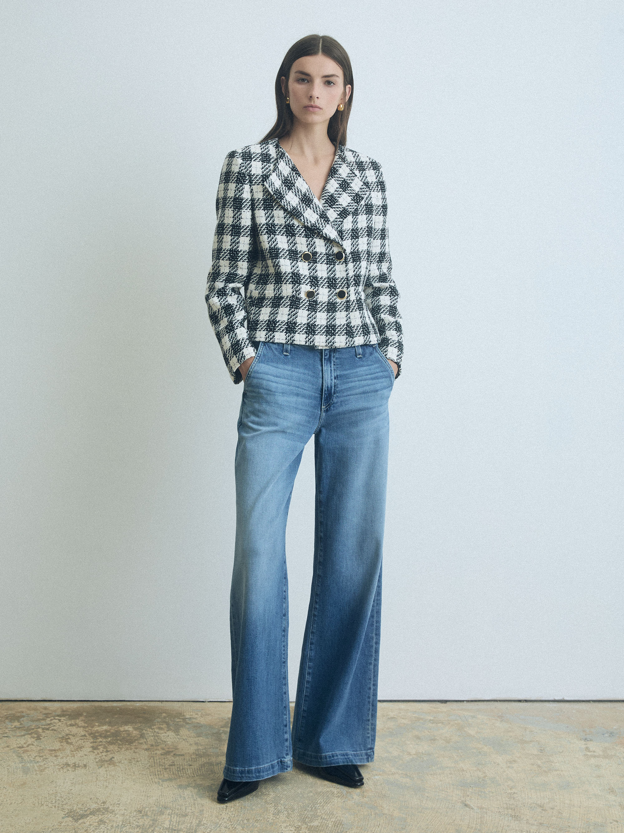 Woman wearing a checkered blazer and blue jeans against a plain background