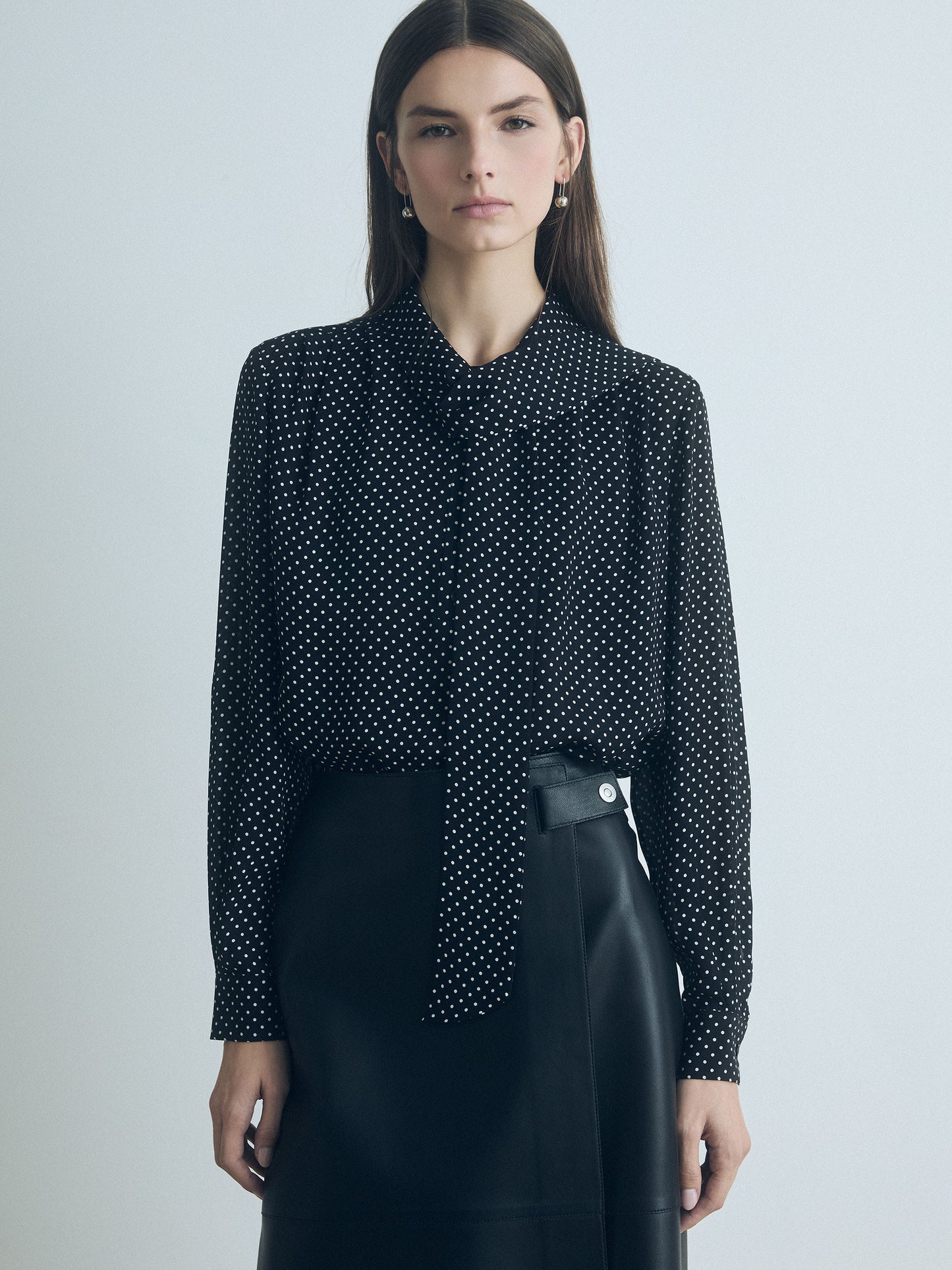 Model wearing a black and white silk blouse with long sleeves, pleats, and neck tie. Straight fit, unlined, with button closure 