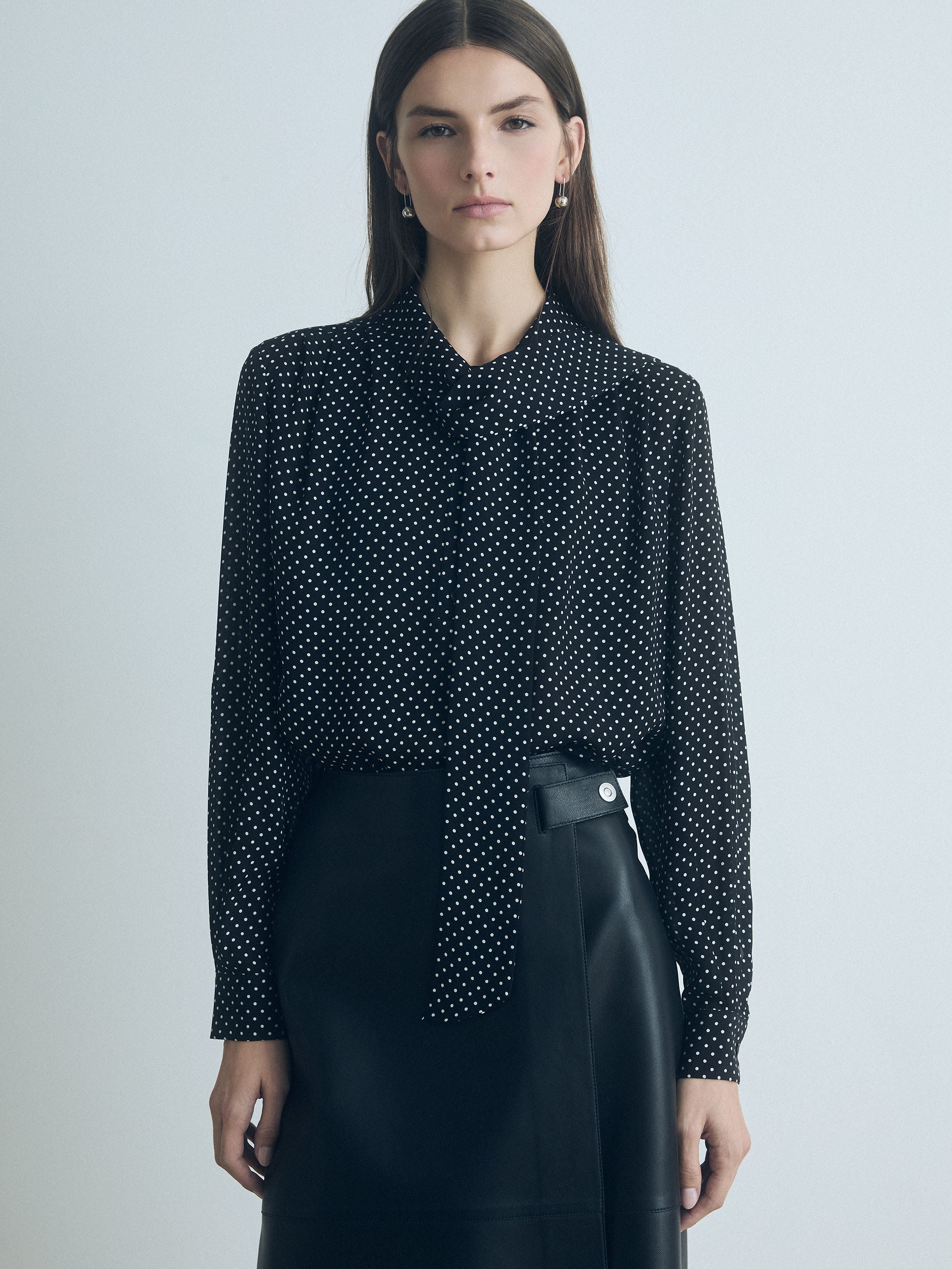 Model wearing a black and white silk blouse with long sleeves, pleats, and neck tie. Straight fit, unlined, with button closure 