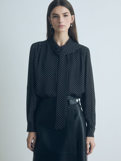 Model wearing a black and white silk blouse with long sleeves, pleats, and neck tie. Straight fit, unlined, with button closure 