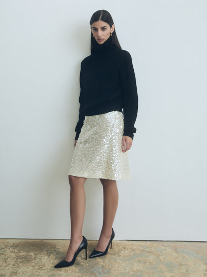 Woman wearing a black turtleneck and Oyster straight sequin skirt with clean waist and back slit from Judith and Charles