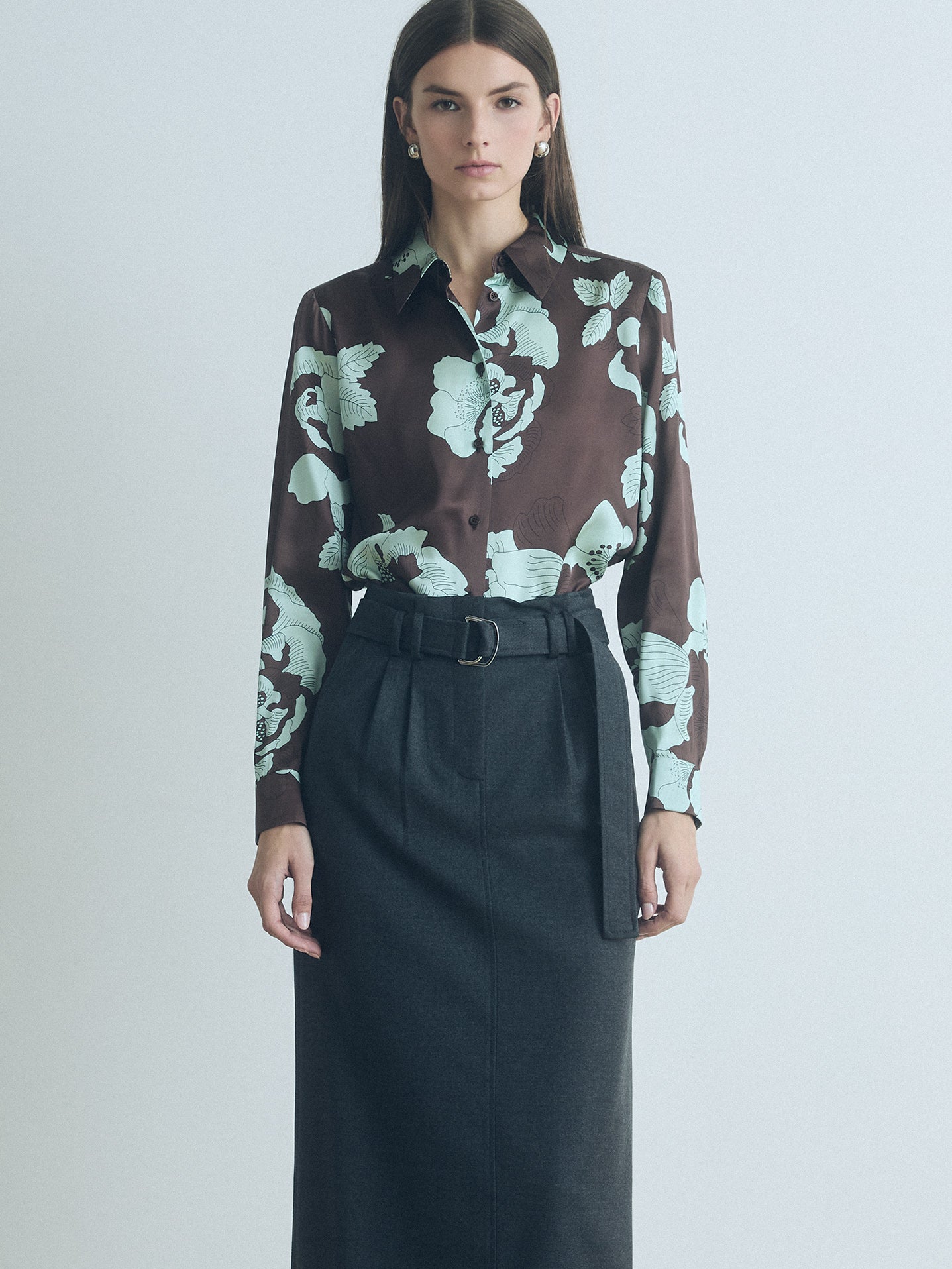 Woman wearing a floral chocolate judith and charles silk blouse and black skirt on a light gray background