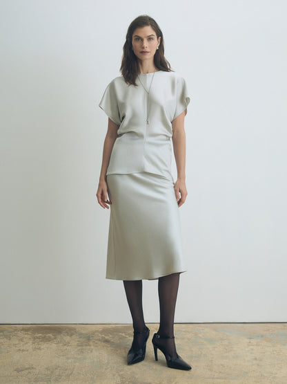 Model wearing a pearl textured satin bias long skirt with clean waistband and fluid drape, styled with a matching satin blouse. Minimalist, elegant look