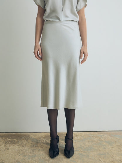 Person wearing a light-colored pearl skirt and top against a plain background