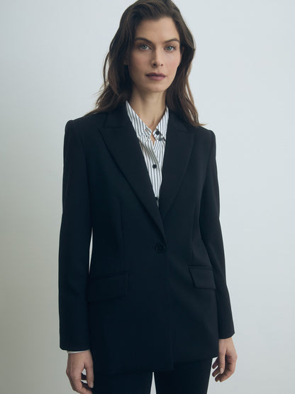 Woman wearing a black blazer over a striped shirt on a plain background