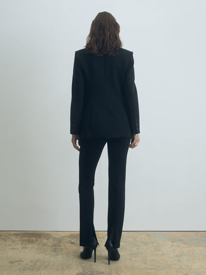 Person wearing a black suit standing against a plain white wall.