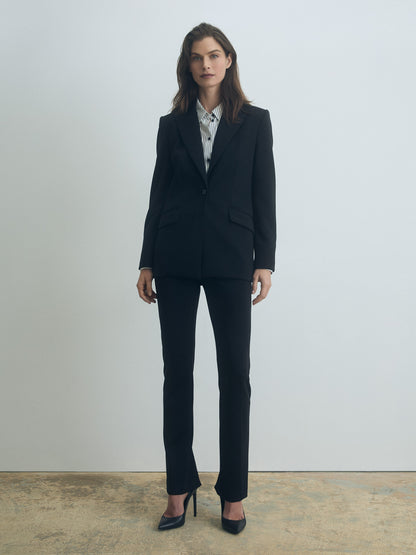 Woman wearing a black suit standing against a plain background