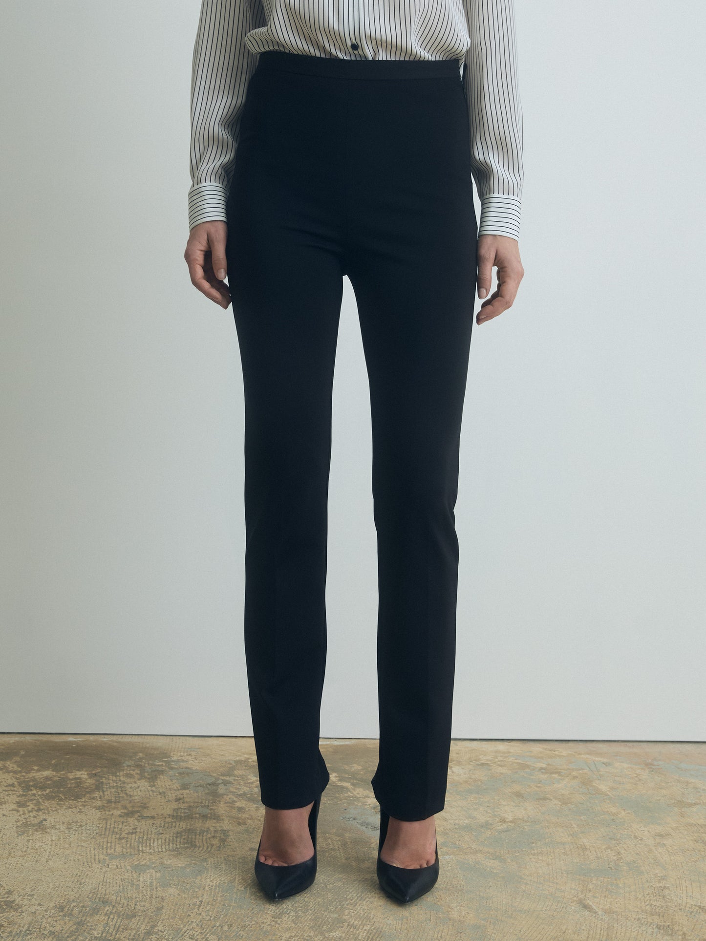 Person wearing black pants and a striped shirt against a plain background