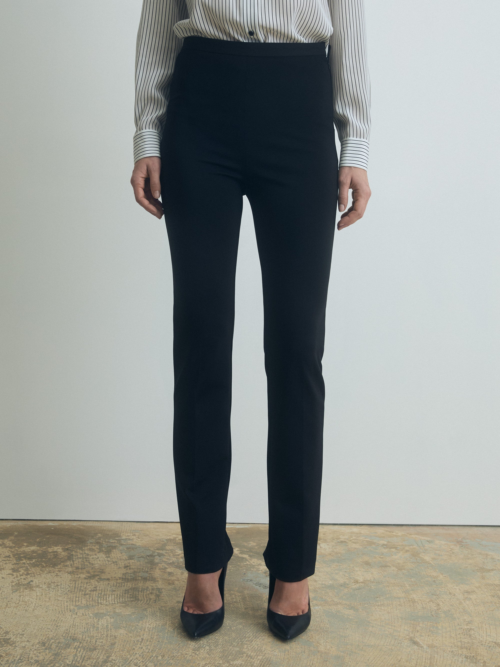 Person wearing black pants and a striped shirt against a plain background