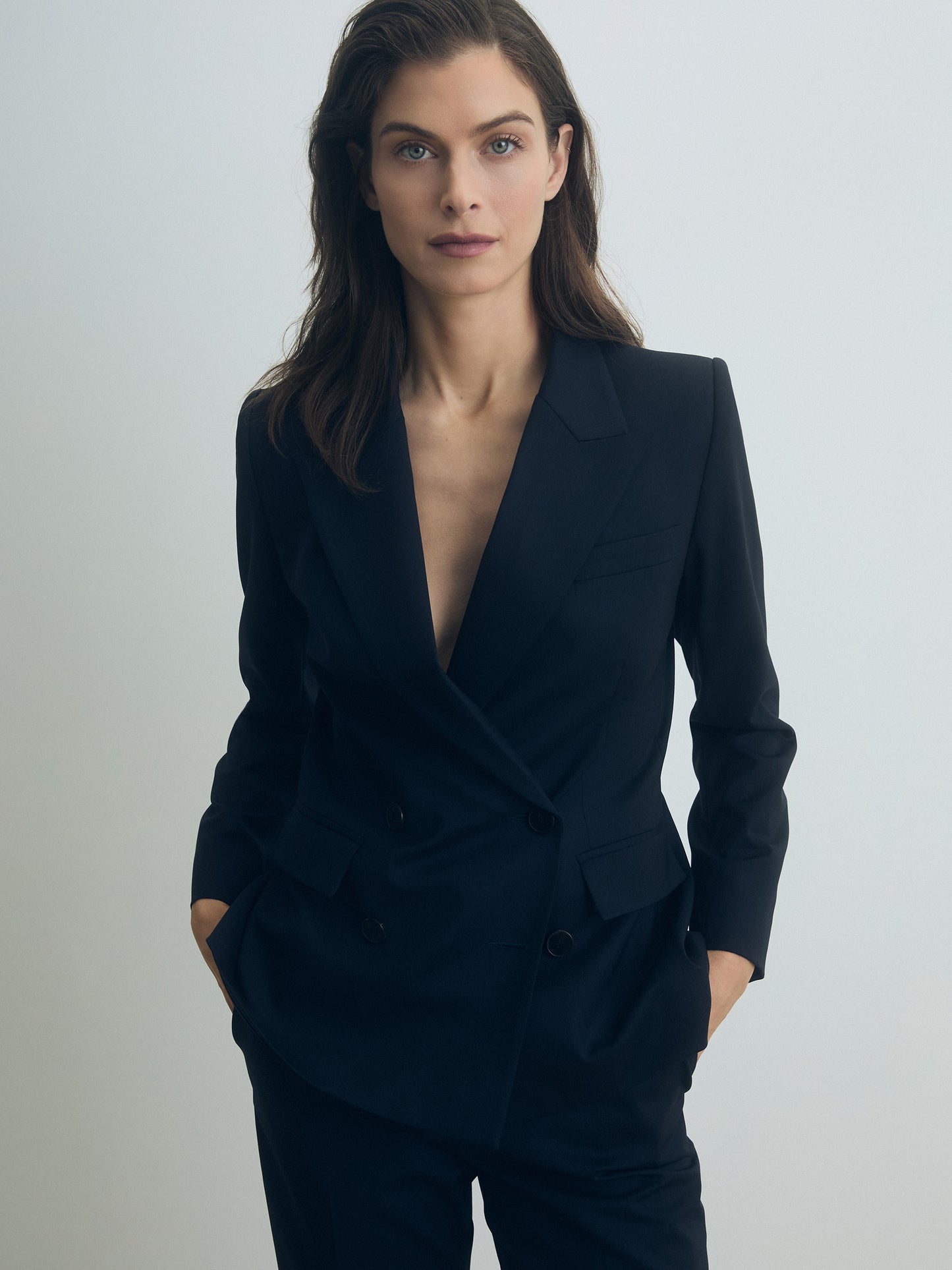 Woman wearing a navy double breasted suit against a plain background