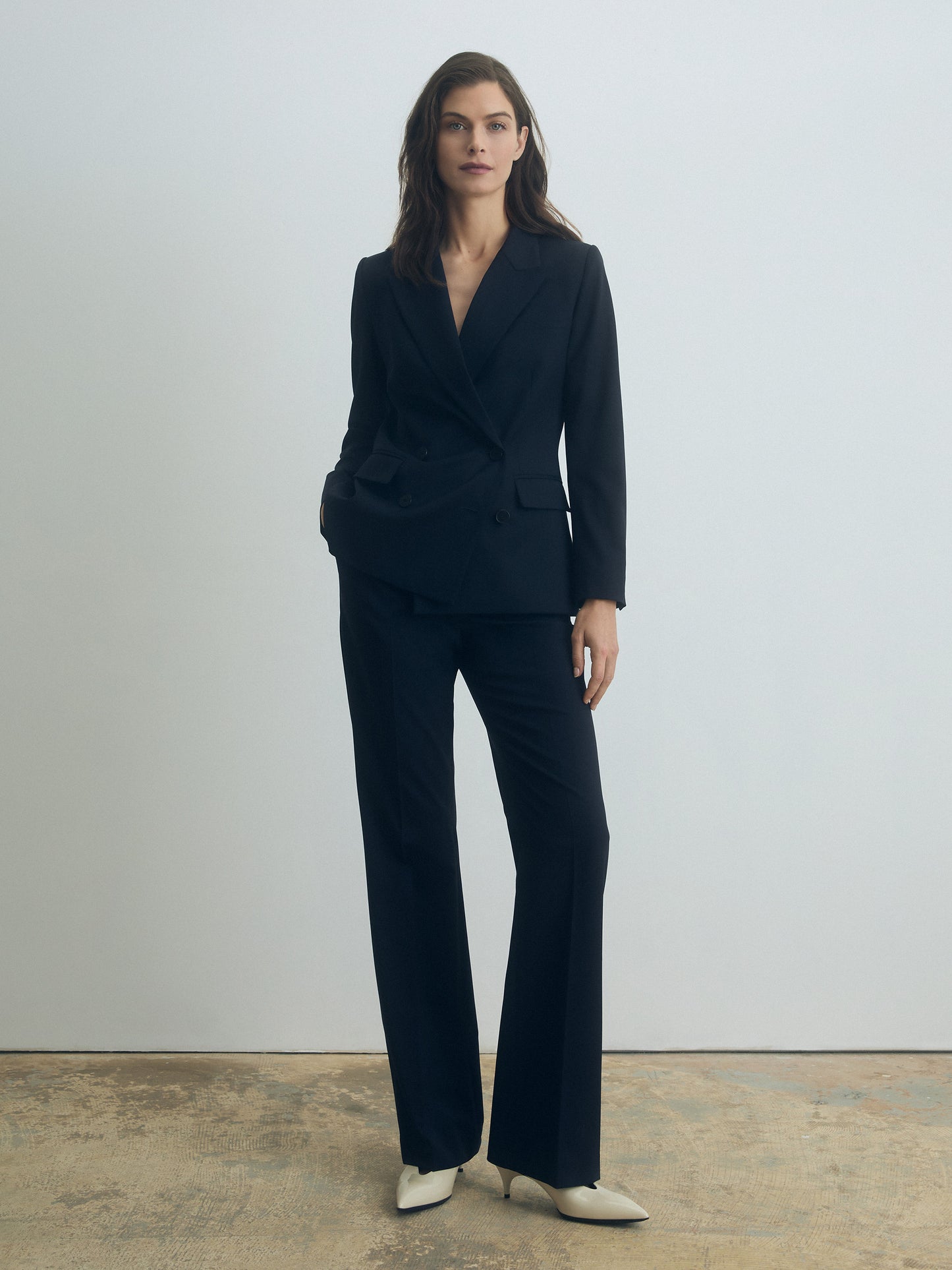Woman wearing a navy blue suit standing against a plain background