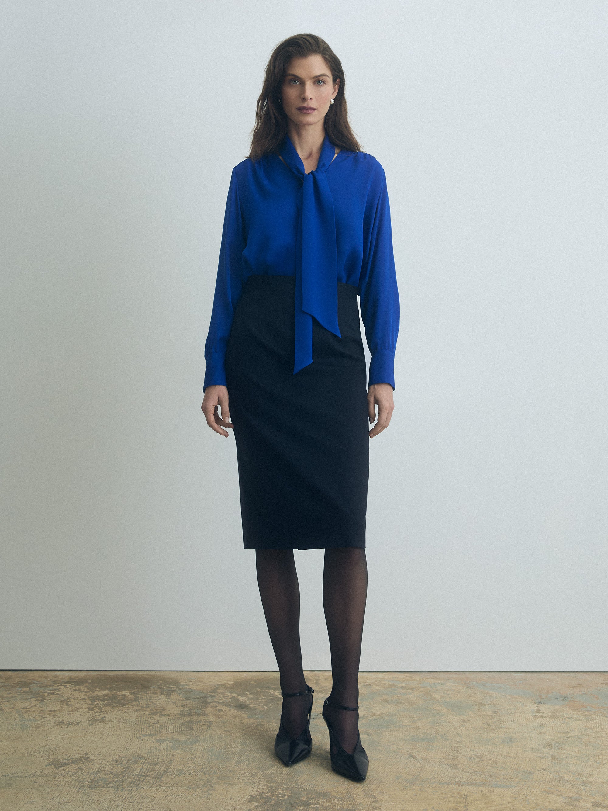 Woman wearing a blue blouse and black skirt against a plain background