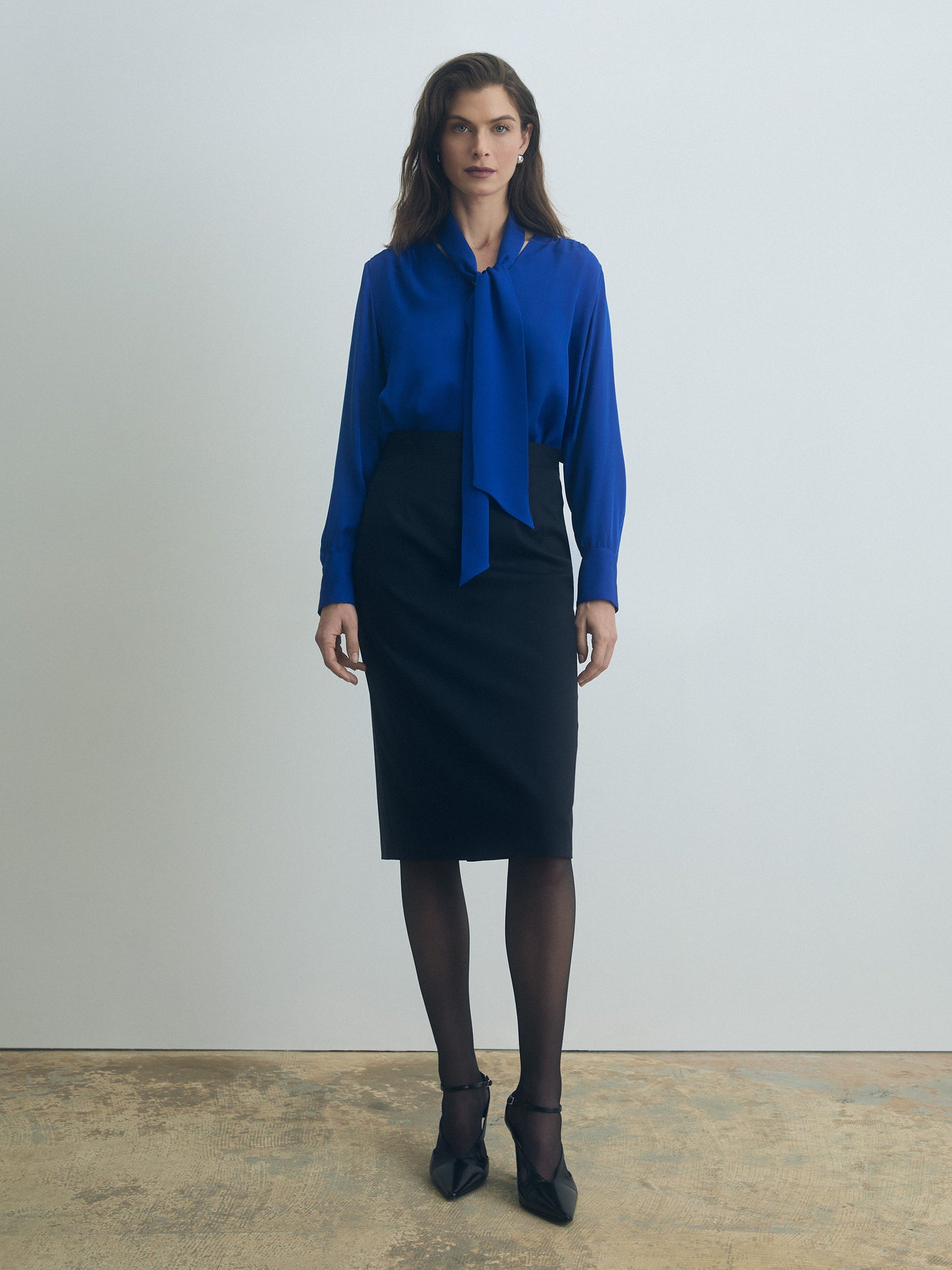 Woman wearing a blue ocean cavaiiere blouse and navy skirt against a plain background