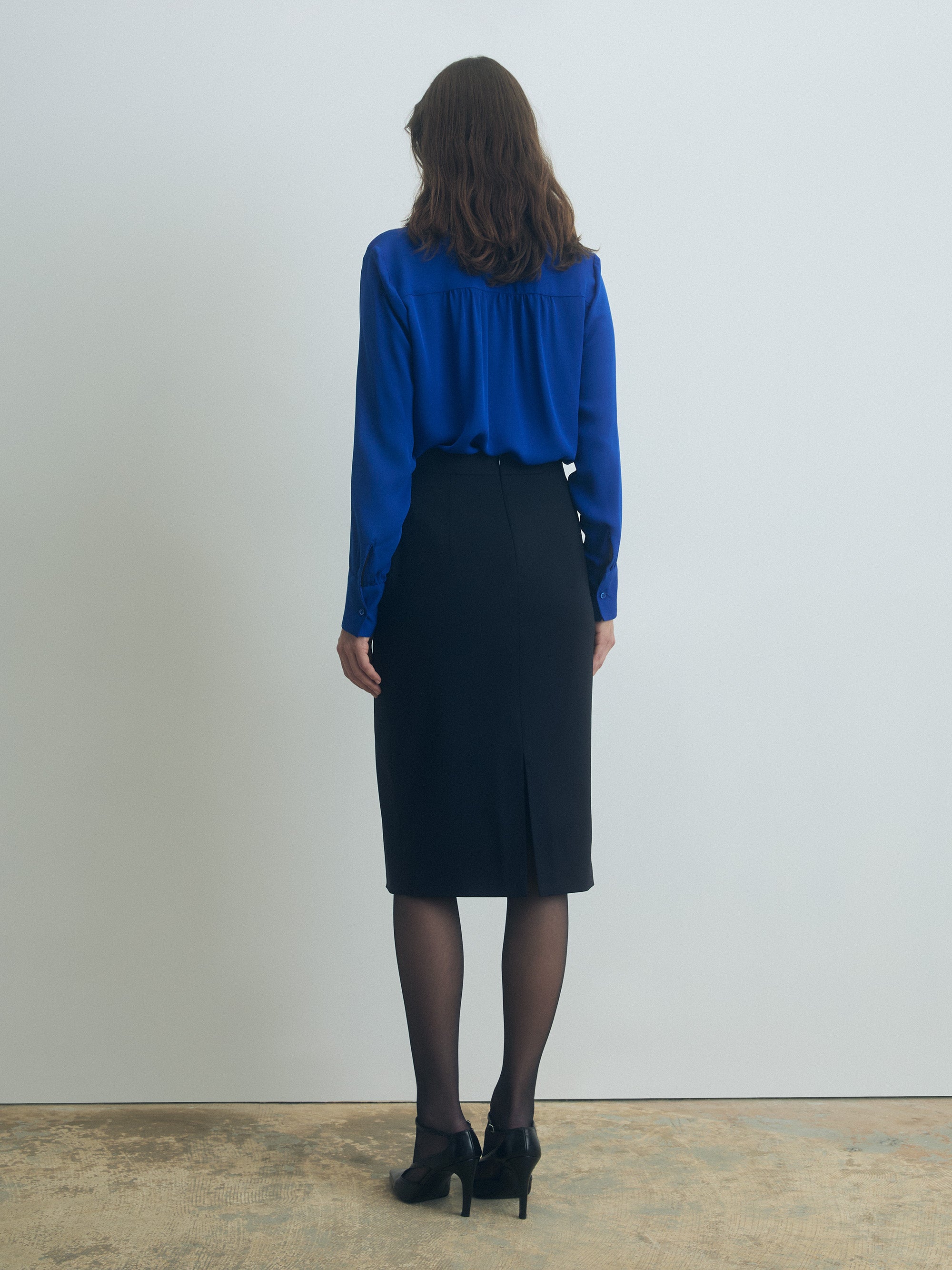 Person wearing a blue blouse and black skirt against a plain background