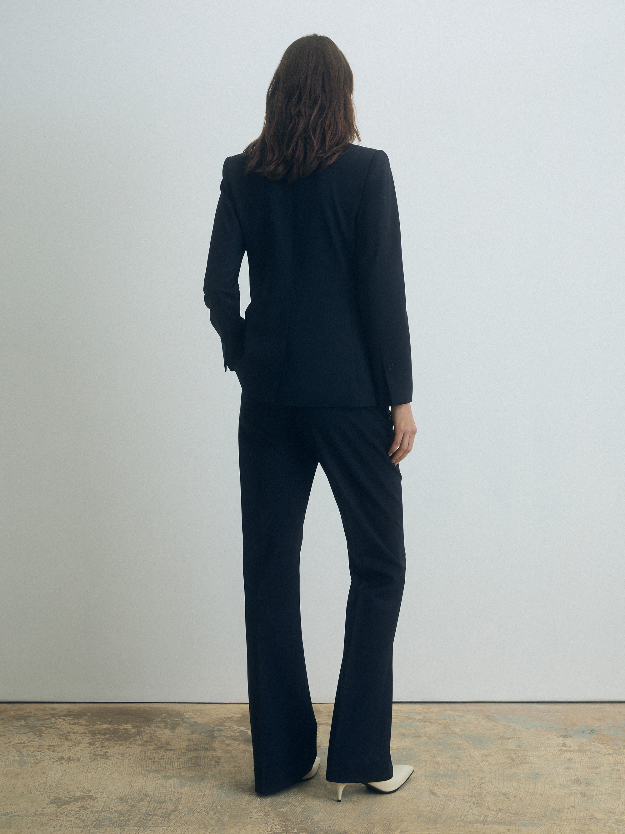 Woman wearing a navy suit standing against a plain white wall.