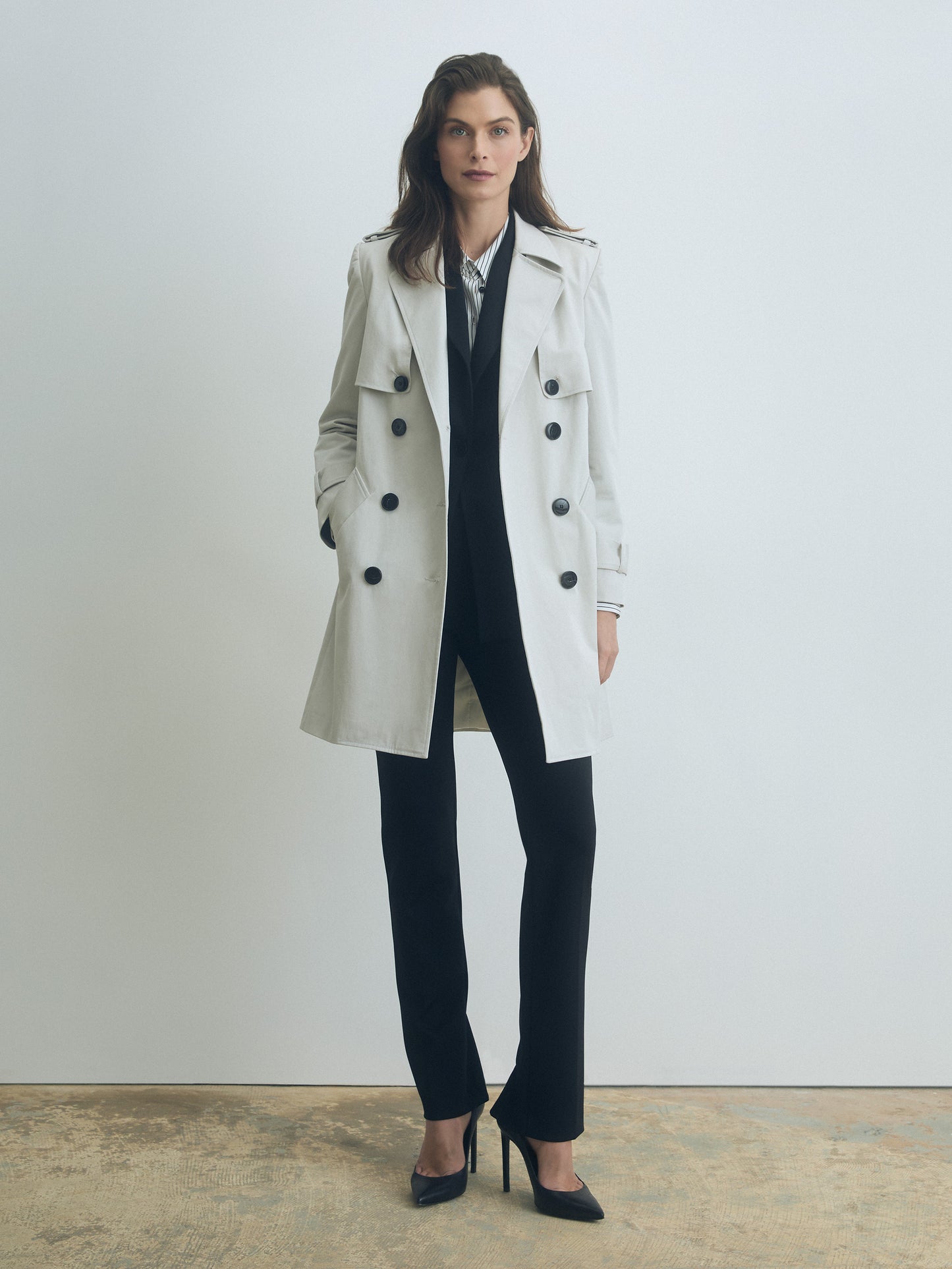 Woman wearing a pearl trench coat over a dark outfit against a plain background