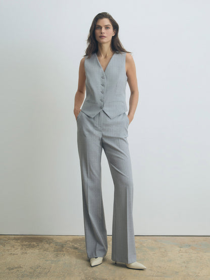 Woman wearing a gray vest and pants set against a plain background