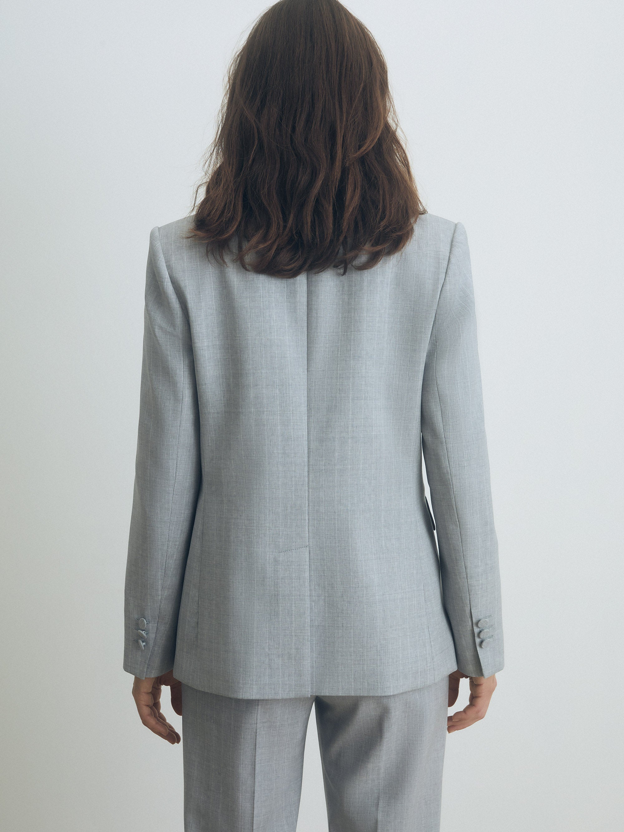 Person wearing a gray pinstripe suit against a white background