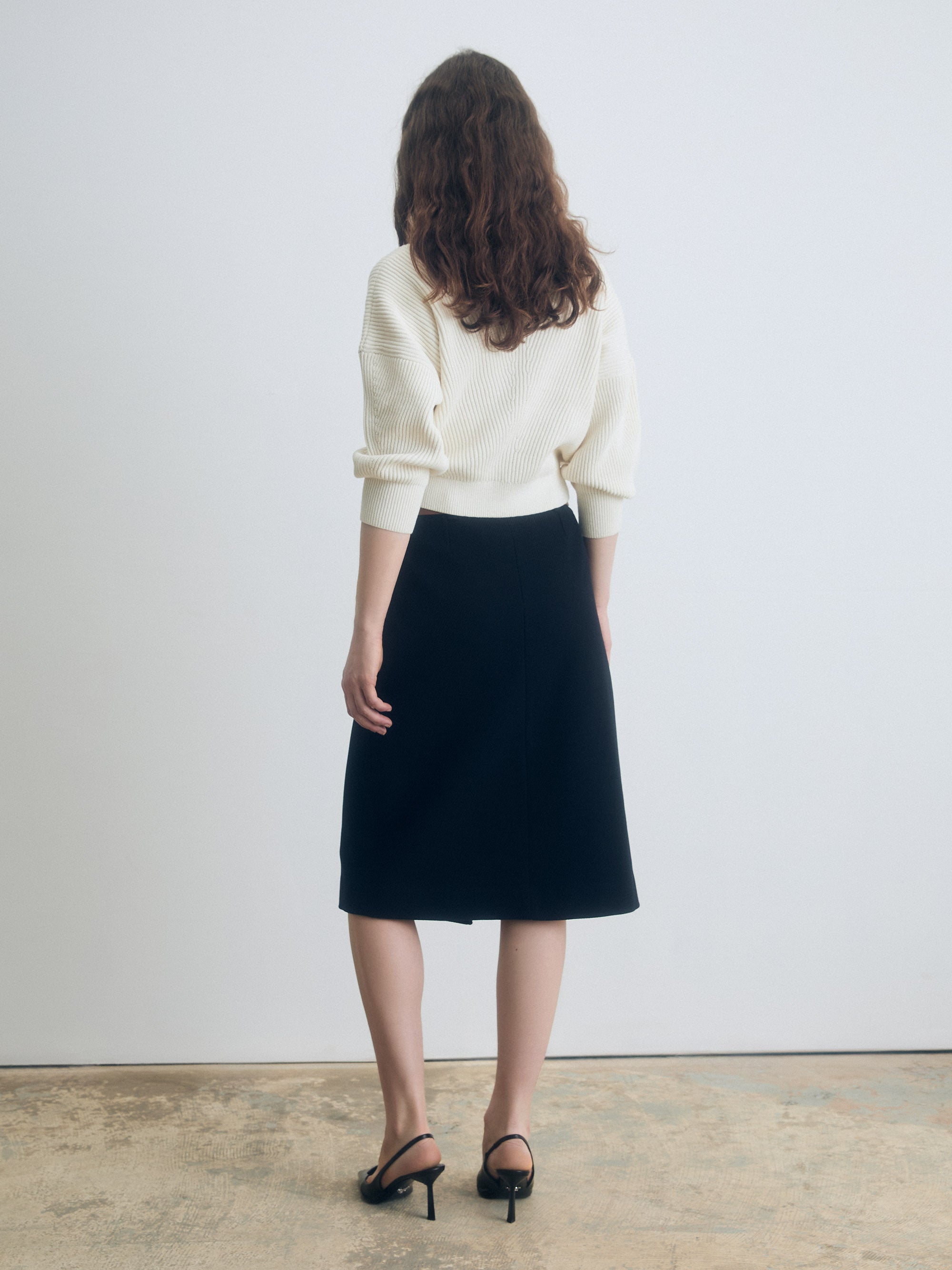 Back view of a navy A‑line skirt styled with a cream knit top and black heeled sandals